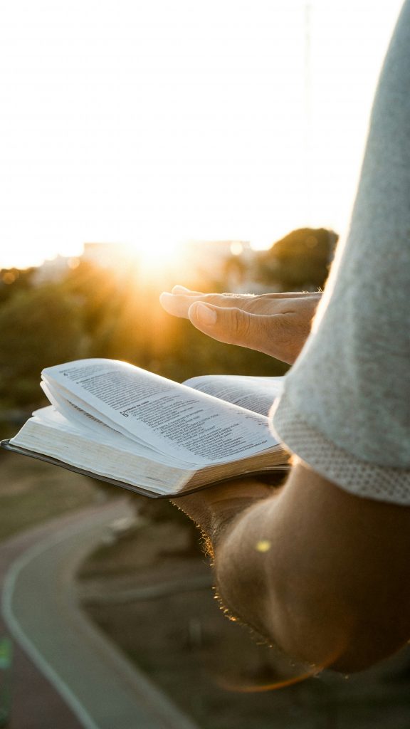 Person sitzt mit Bibel in der Hand und betet in der Natur - Symbol für Ruhe und Gottesnähe